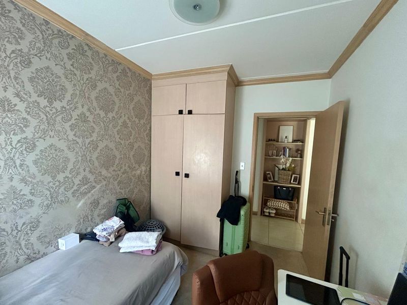 A bedroom featuring a built-in wardrobe, decorative wallpaper, and crown molding, with an adjacent storage or closet area visible through the doorway.
