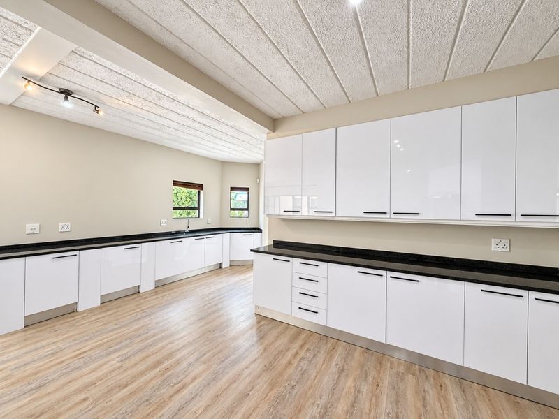 Spacious, modern kitchen featuring high-gloss white cabinetry, contrasting black granite countertops, and durable laminate wood flooring in a clean, open-plan layout.