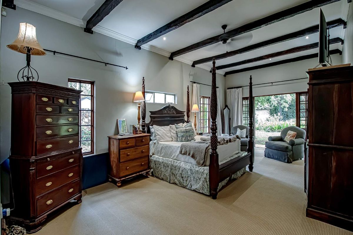 Spacious bedroom featuring exposed timber ceiling beams, neutral carpeting, and direct access to the garden through glass-paned doors.