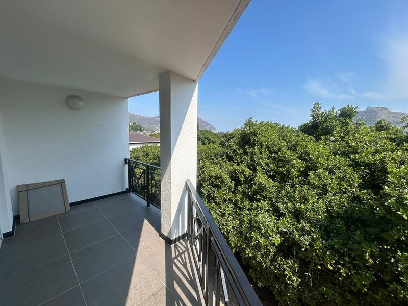 A spacious covered balcony featuring modern tiled flooring, a secure metal balustrade, and pleasant views of the surrounding greenery and distant mountains.