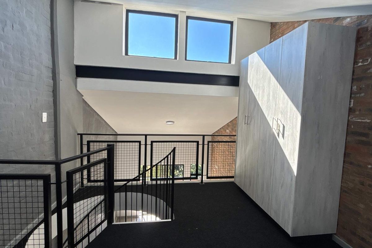A mezzanine level featuring industrial-style metal railings, exposed brickwork, high ceilings with clerestory windows, and built-in cabinetry.