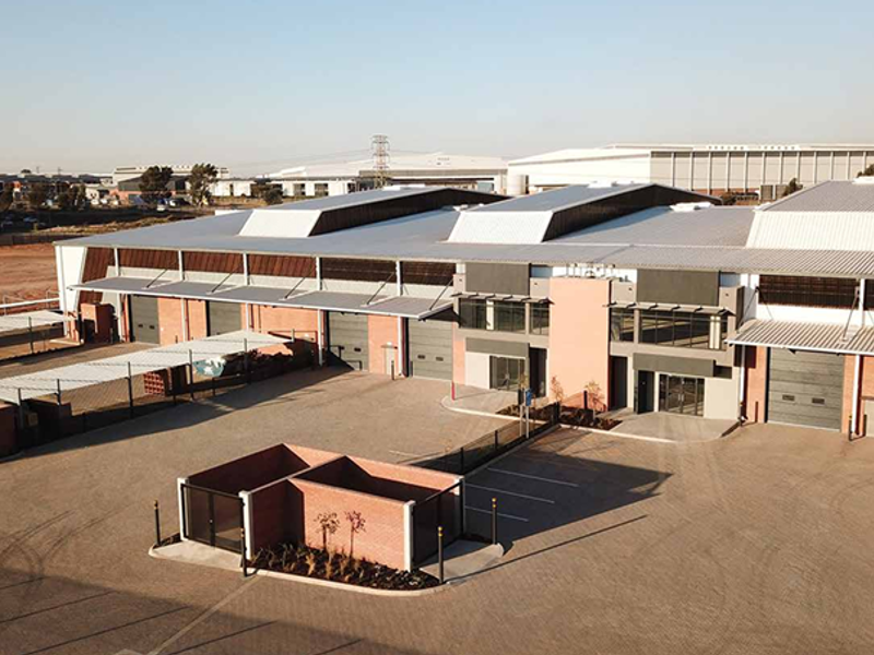 Aerial view of a modern industrial warehouse complex featuring multiple roller shutter doors, paved yard area, and secure perimeter fencing.