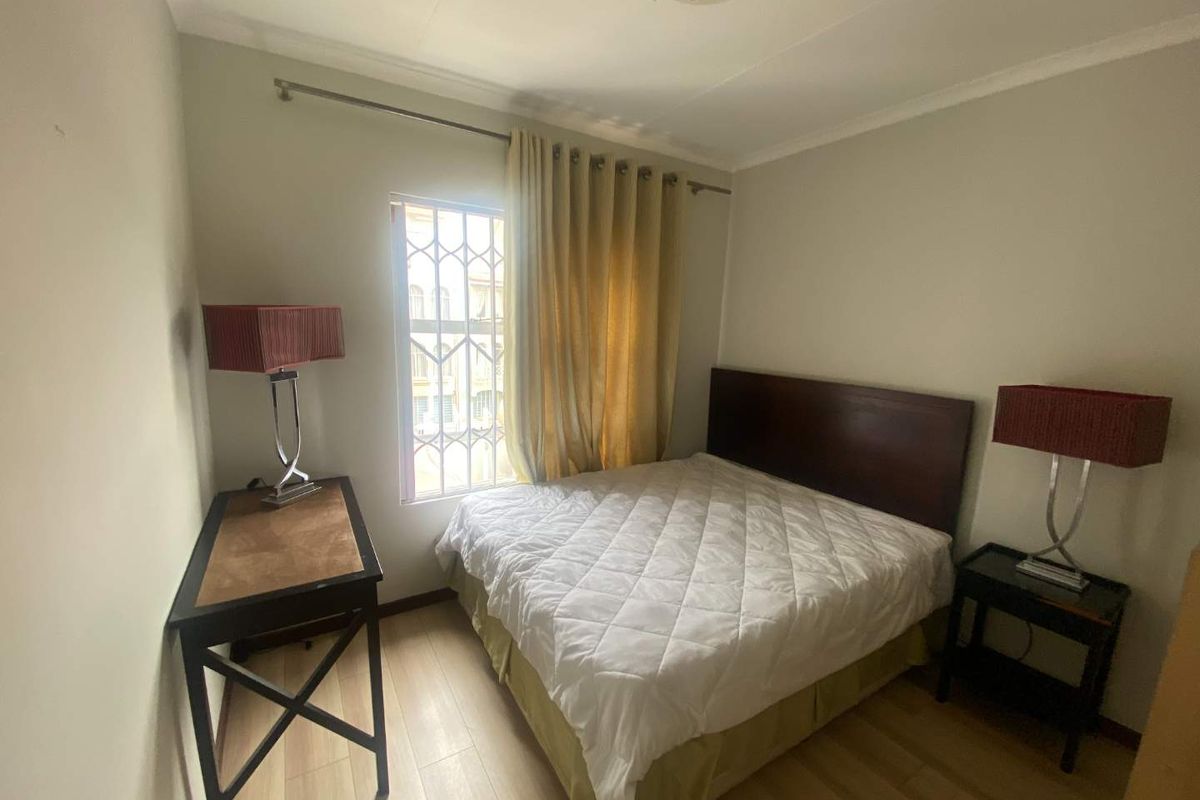 A functional bedroom featuring laminate flooring, a window with security bars, and a ceiling-mounted light fixture.