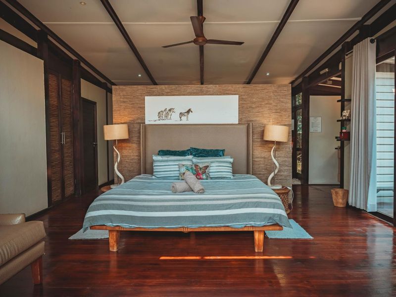 Spacious bedroom featuring rich hardwood flooring, exposed ceiling beams, a textured feature wall, and large sliding glass doors providing natural light.
