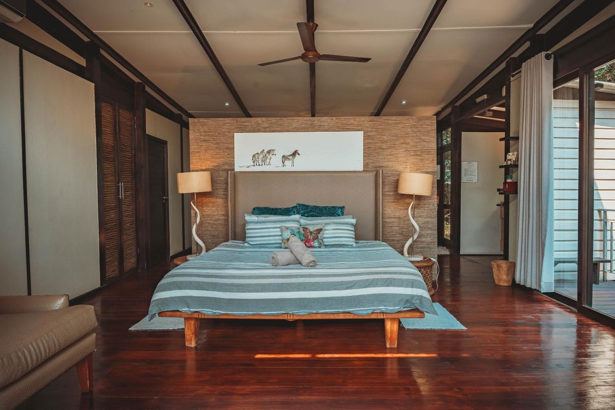 Spacious bedroom featuring rich hardwood flooring, exposed ceiling beams, a textured feature wall, and large sliding glass doors providing natural light.