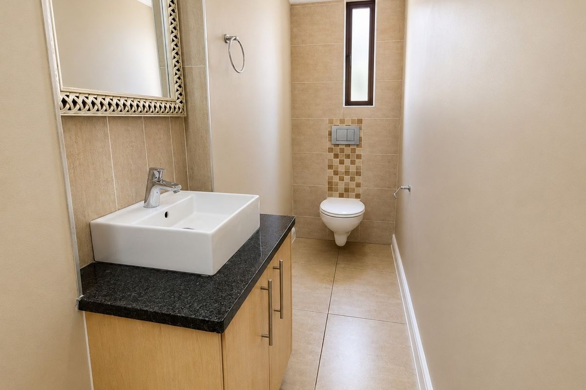 A clean and modern guest bathroom featuring a wall-mounted toilet, vanity cabinet with granite countertop, and neutral tiled finishes.