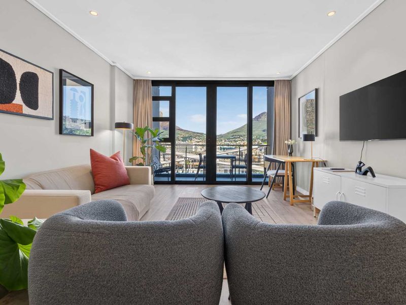 Modern living room featuring laminate flooring, recessed lighting, and large sliding glass doors opening to a balcony with scenic mountain views.
