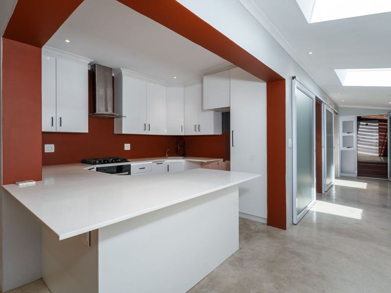 Modern kitchen featuring white cabinetry, stone countertops, gas hob, and polished concrete floors, illuminated by natural light from overhead skylights.