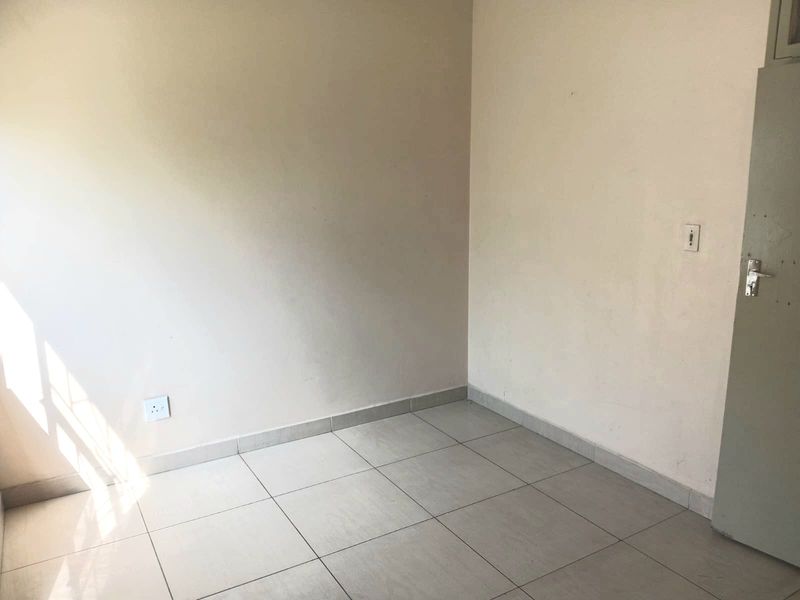 A vacant bedroom featuring neutral tiled flooring, clean wall finishes, and a standard internal door, offering a blank canvas for personalization.