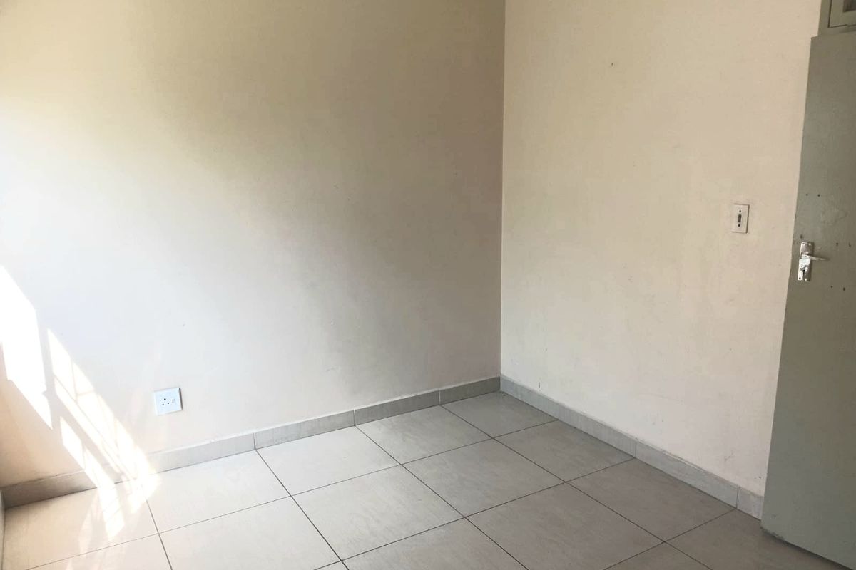 A vacant bedroom featuring neutral tiled flooring, clean wall finishes, and a standard internal door, offering a blank canvas for personalization.