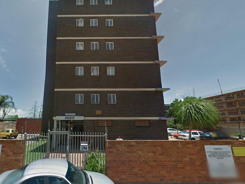 Front exterior view of a multi-story brick apartment building featuring a gated entrance and perimeter security fencing.