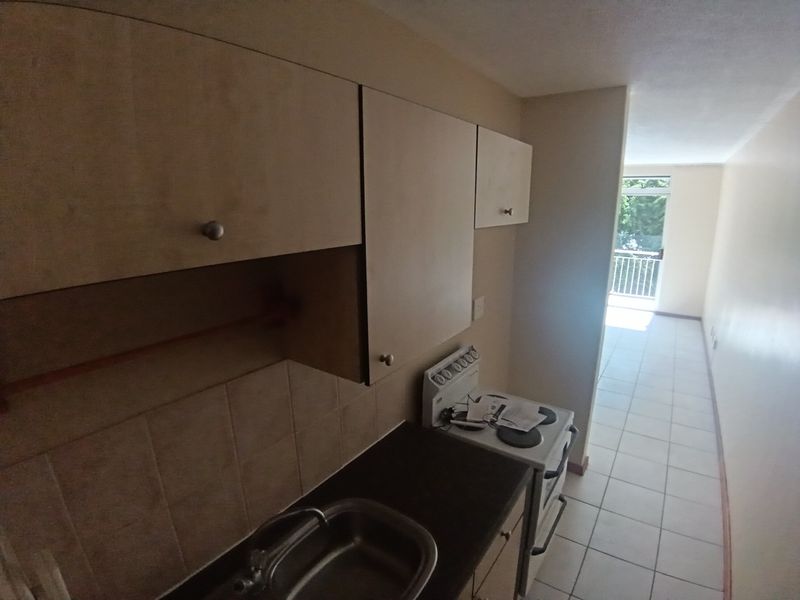A compact kitchen featuring built-in cabinetry, a stainless steel sink, and a freestanding stove, leading into an open-plan living area with balcony access.