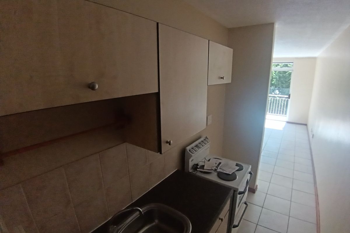 A compact kitchen featuring built-in cabinetry, a stainless steel sink, and a freestanding stove, leading into an open-plan living area with balcony access.