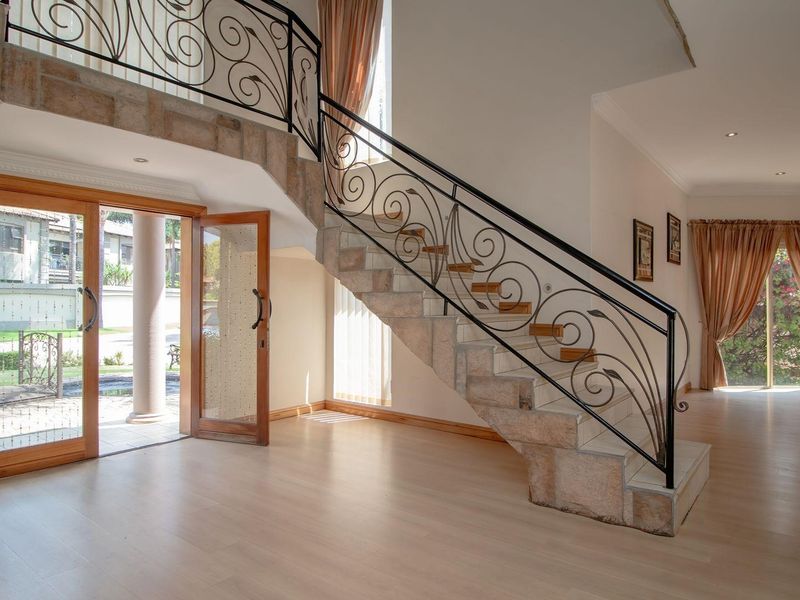 Spacious entrance hall featuring a grand stone staircase with decorative wrought iron railings, light laminate flooring, and direct access to the exterior.