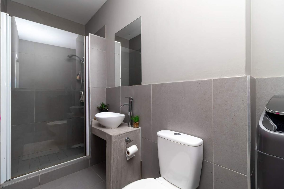 Modern bathroom featuring a glass-enclosed shower, contemporary vessel sink with chrome faucet, and neutral grey wall and floor tiling.