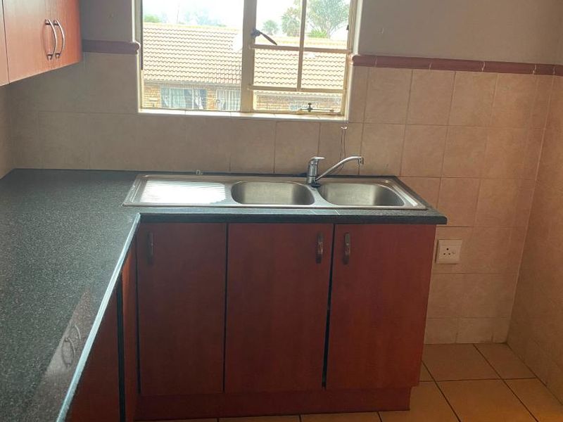 A functional kitchen area featuring laminate cabinetry, a stainless steel double sink, and tiled finishes, ready for a modern update.