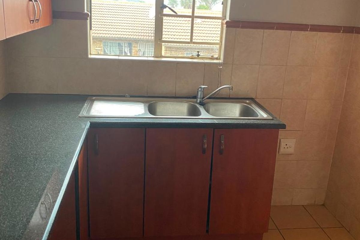 A functional kitchen area featuring laminate cabinetry, a stainless steel double sink, and tiled finishes, ready for a modern update.