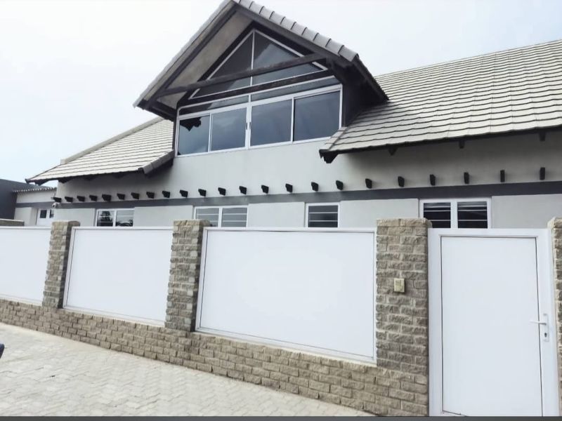 Front elevation of a house featuring a tiled roof, exposed timber rafters, and a secure brick boundary wall with a pedestrian gate.