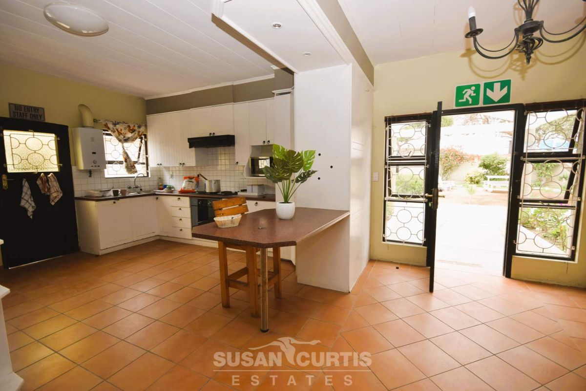 A functional kitchen featuring white cabinetry, tiled flooring, and direct access to the rear outdoor area through a security-fitted door.