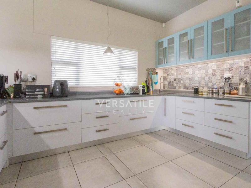 Modern kitchen featuring white lower cabinetry, light blue upper cabinets, stone countertops, decorative tiled backsplash, and large format floor tiles.