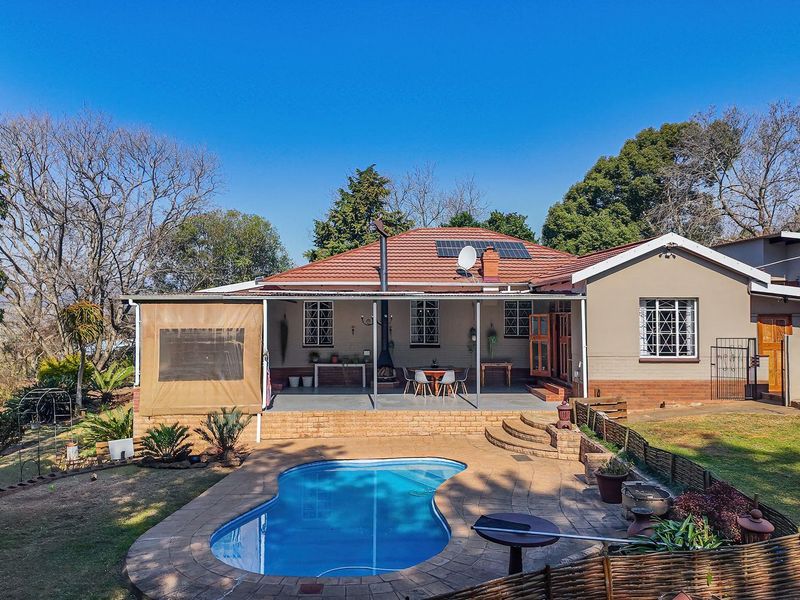 Rear view of the property featuring a swimming pool, paved patio area, and a covered outdoor entertainment space with a fireplace.