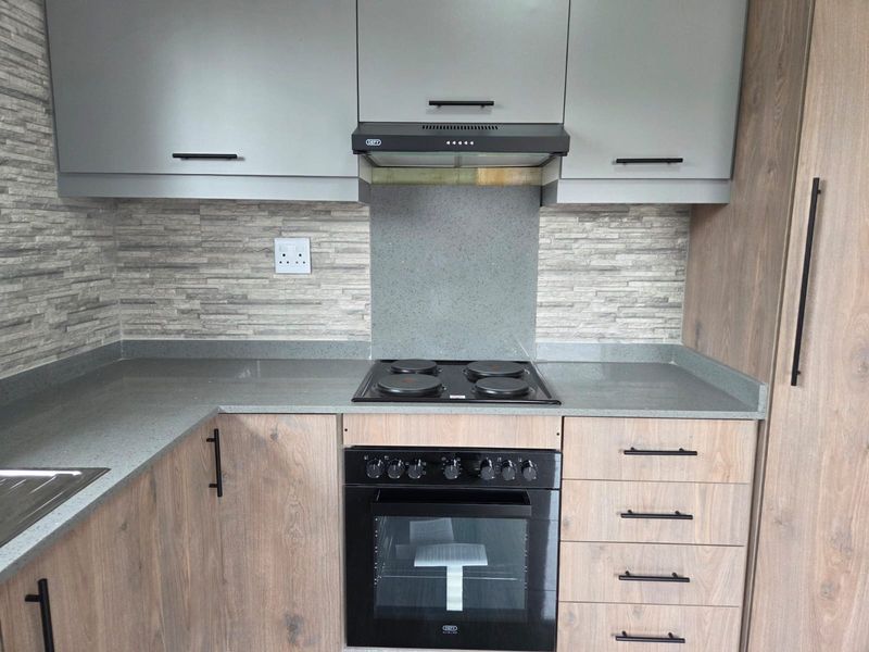 Modern kitchen featuring wood-grain cabinetry, stone countertops, a built-in electric oven, hob, and extractor fan with a stylish stone tile backsplash.