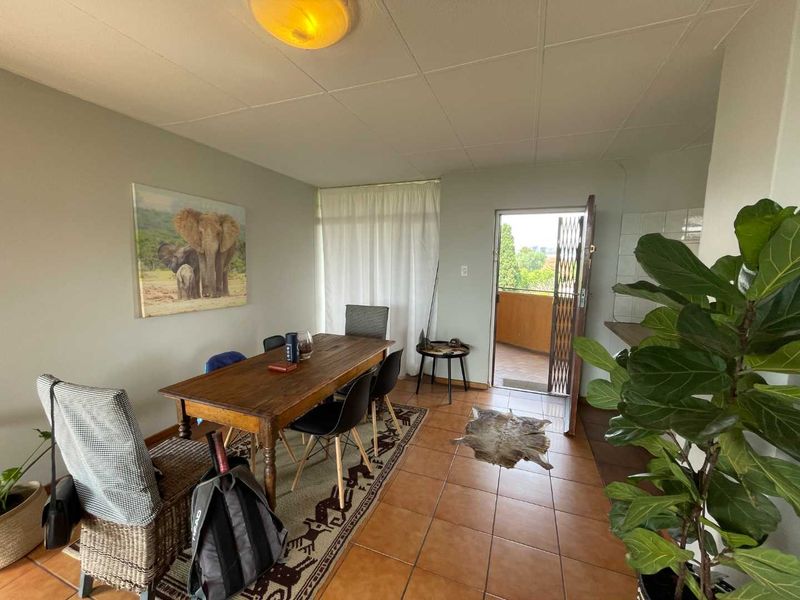 Open plan living and dining area featuring tiled flooring, a ceiling light fixture, and direct access to an outdoor balcony through a security gate.