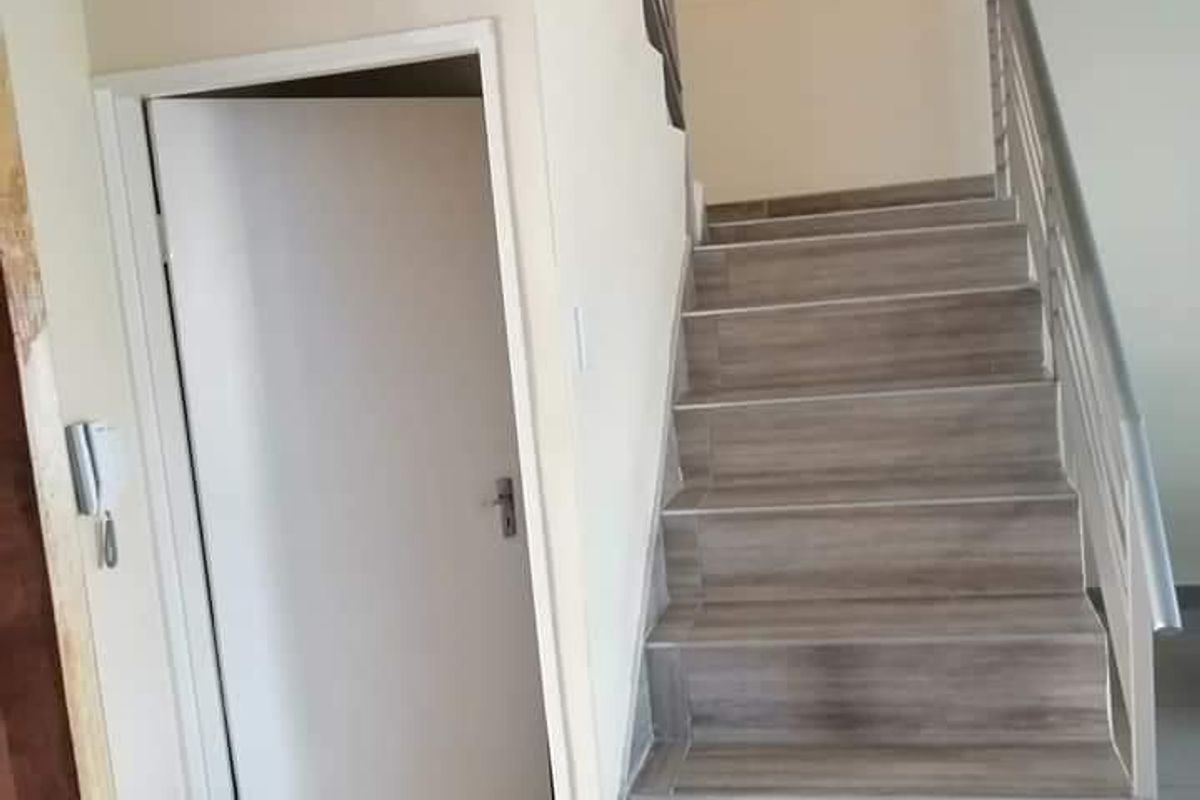 A bright entrance hallway featuring a tiled staircase with a metal handrail and an intercom system, leading to an upper level.