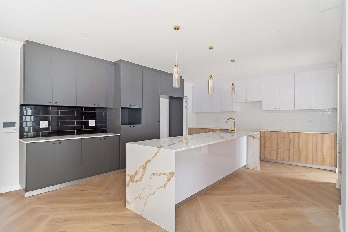 Modern kitchen featuring a large stone island, contrasting grey and white cabinetry, subway tile splashbacks, and elegant herringbone timber flooring.