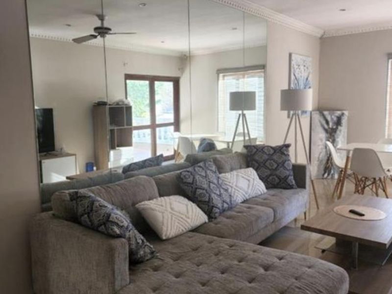 A well-maintained living room featuring tiled flooring, crown molding, recessed lighting, a ceiling fan, and a large feature wall mirror.