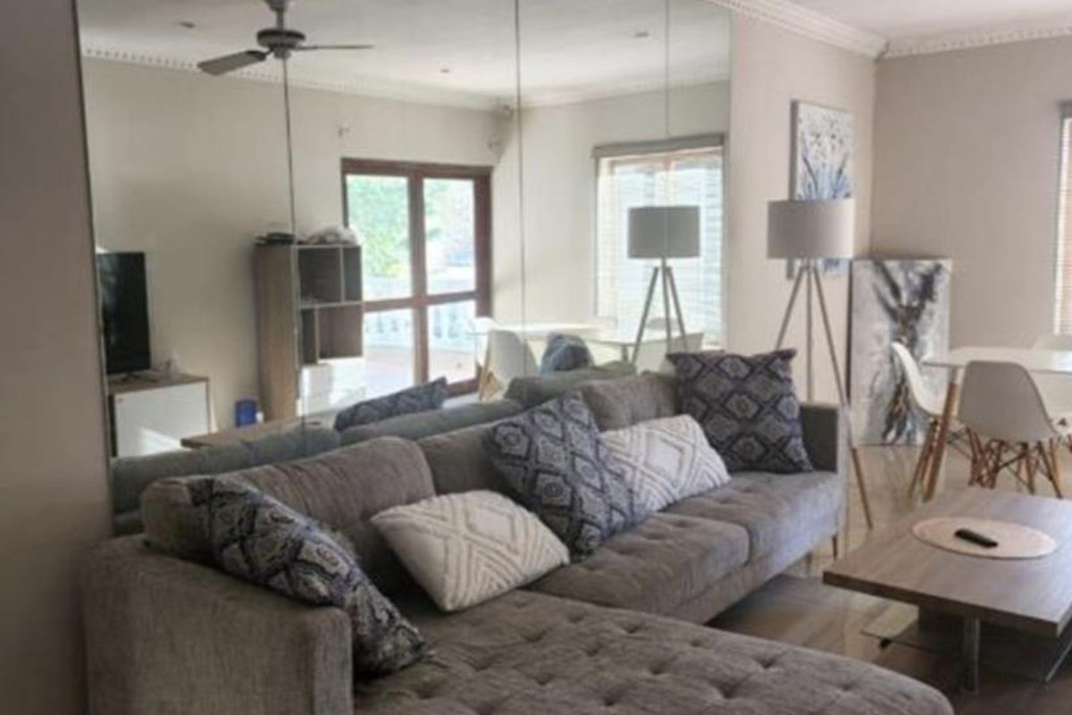 A well-maintained living room featuring tiled flooring, crown molding, recessed lighting, a ceiling fan, and a large feature wall mirror.