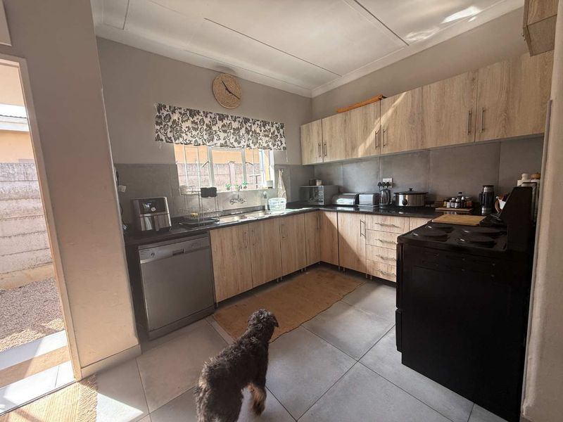 A functional kitchen featuring light wood-tone cabinetry, dark stone countertops, tiled backsplash, and tiled flooring with direct access to the exterior.