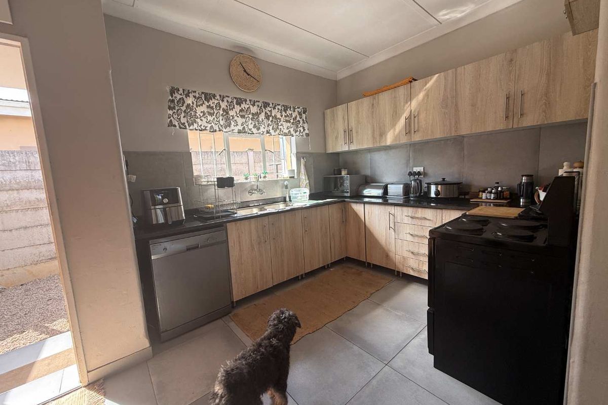 A functional kitchen featuring light wood-tone cabinetry, dark stone countertops, tiled backsplash, and tiled flooring with direct access to the exterior.
