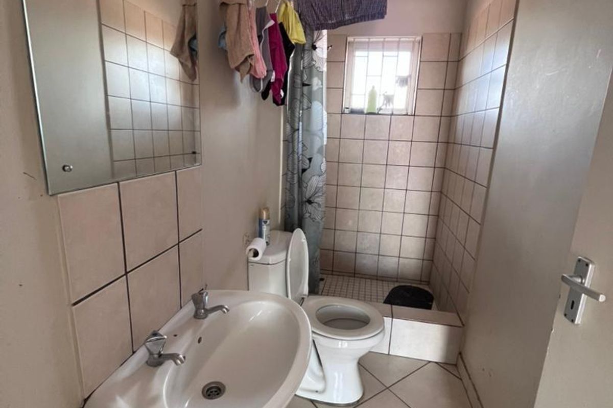 A functional bathroom featuring a wall-mounted basin, toilet, and a tiled shower enclosure with a security-barred window.