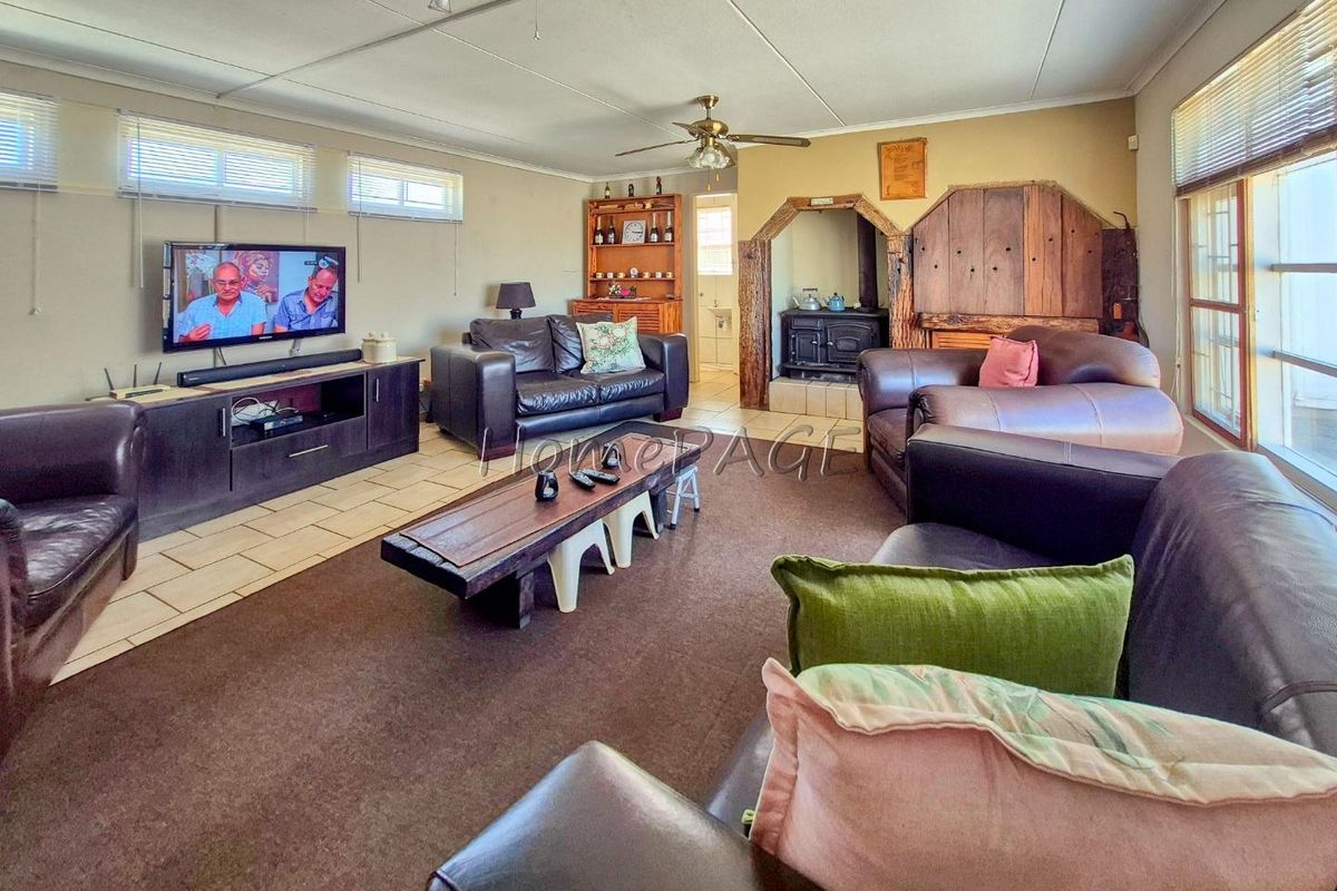 Spacious living room featuring a built-in fireplace with rustic timber surround, tiled and carpeted flooring, and large windows providing natural light.