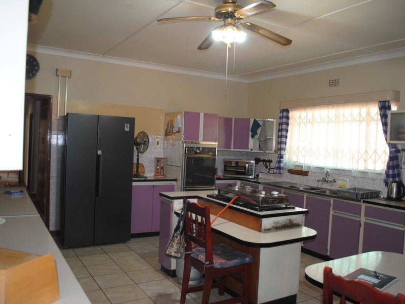 A dated kitchen featuring purple cabinetry, a central island with a cooktop, tiled flooring, and a ceiling fan, offering potential for modern renovation.
