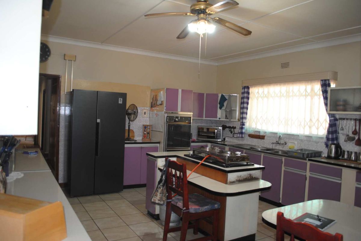 A dated kitchen featuring purple cabinetry, a central island with a cooktop, tiled flooring, and a ceiling fan, offering potential for modern renovation.