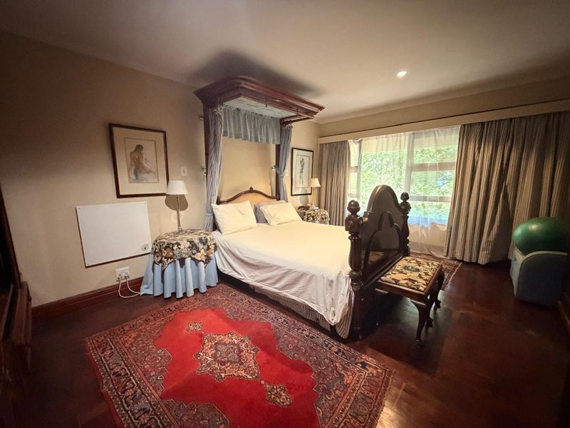 Spacious bedroom featuring polished hardwood flooring, recessed lighting, and a large window with curtain treatments, offering a comfortable and well-lit living space.