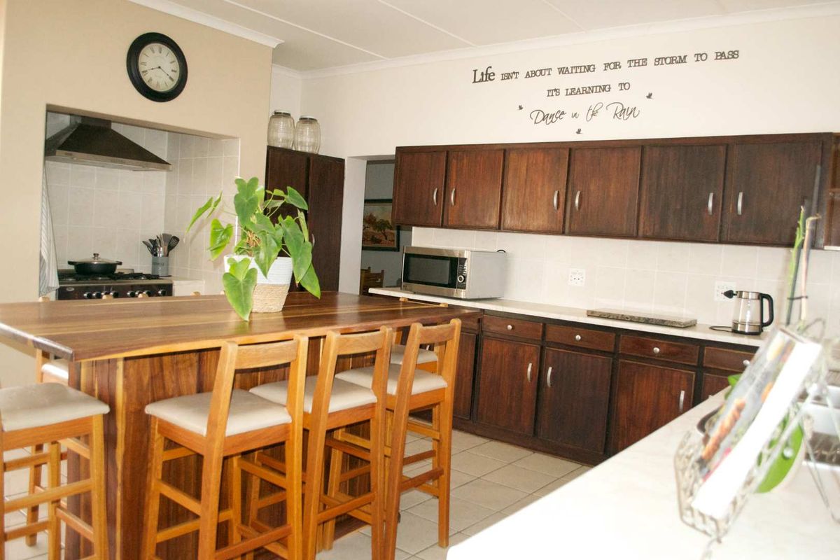 A functional kitchen featuring dark wood cabinetry, a central island with breakfast bar seating, and a separate cooking alcove with an extractor fan.