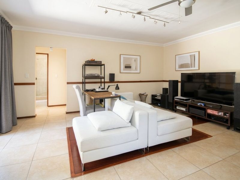 A spacious living room featuring tiled flooring, a ceiling fan, track lighting, and a sliding glass door providing access to the exterior.