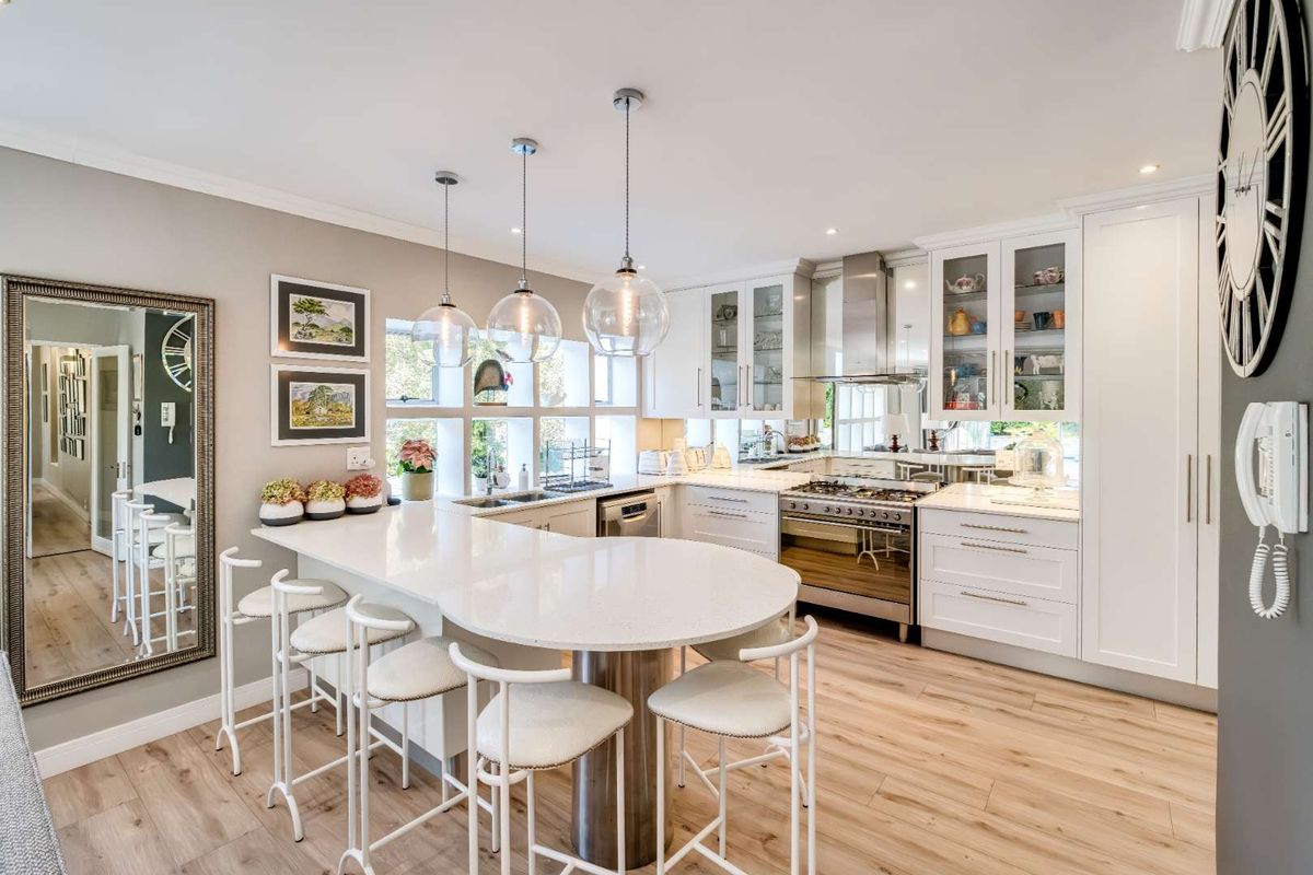 Modern kitchen featuring white cabinetry, quartz countertops, a central breakfast island, gas range, and high-quality finishes throughout.