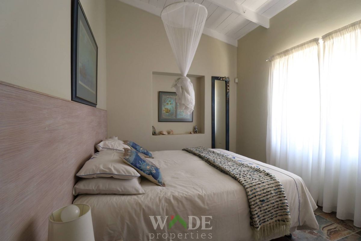 A cozy bedroom featuring a vaulted timber ceiling, a built-in wall niche, and natural light through large windows.