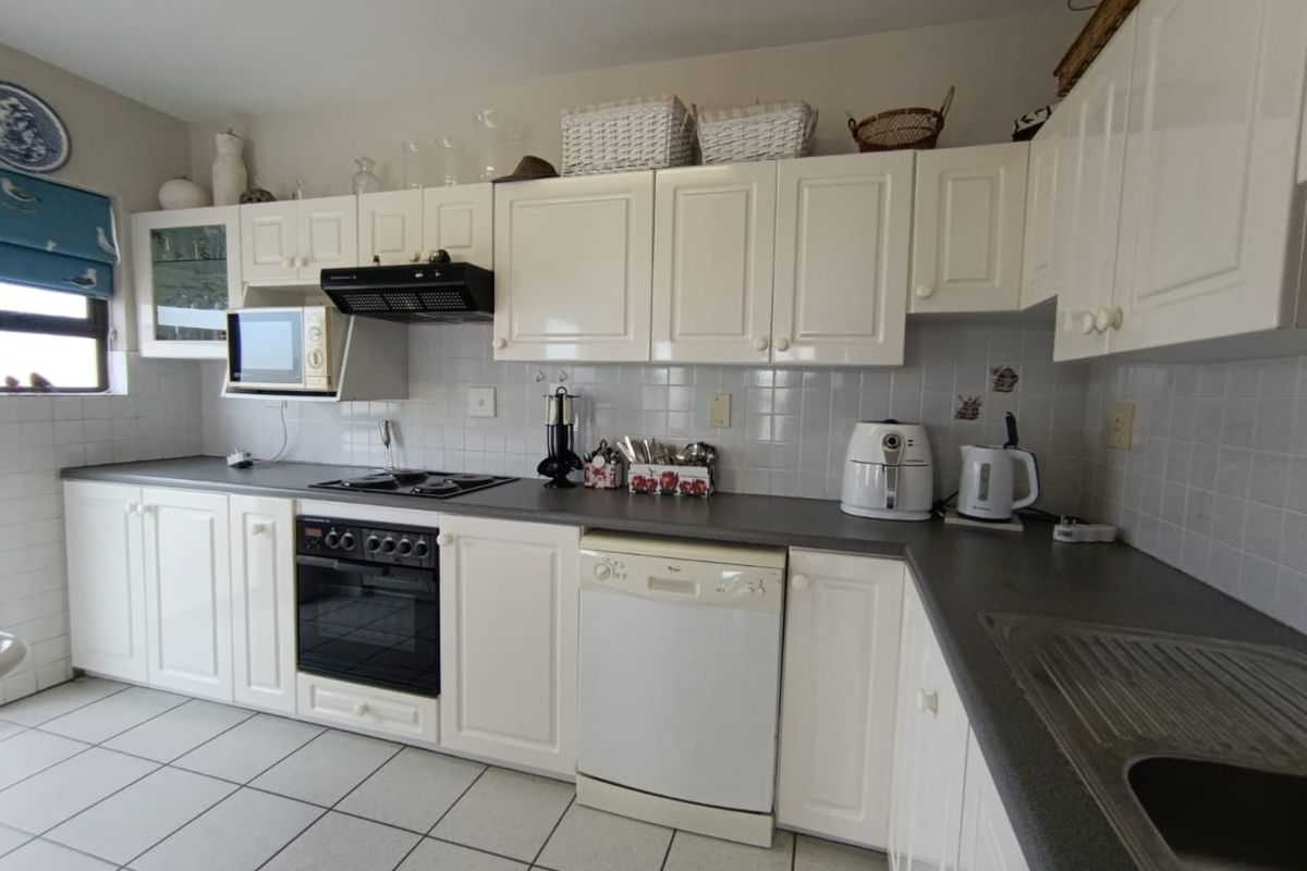 A functional kitchen featuring white cabinetry, dark countertops, tiled backsplash, built-in oven, hob, extractor fan, and integrated dishwasher space.