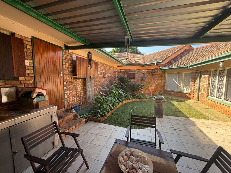 A covered outdoor patio area featuring brick walls, tiled flooring, and direct access to a small garden space.