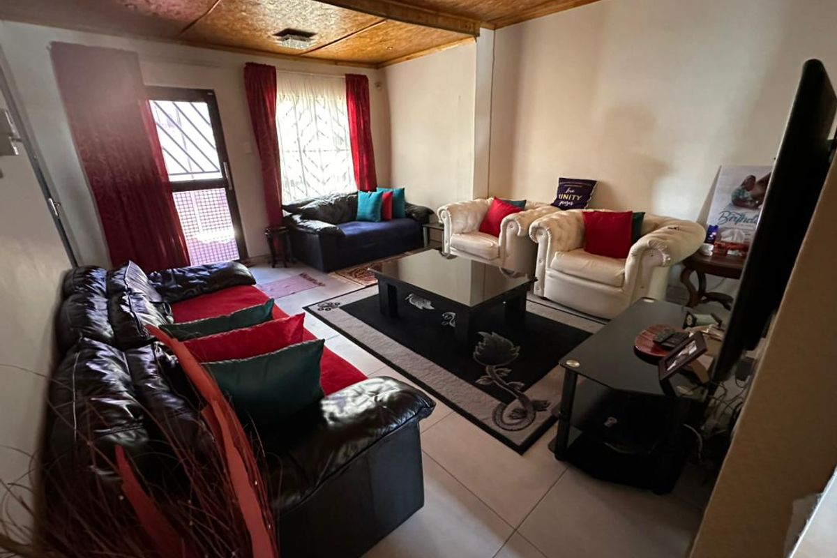 A living room featuring tiled flooring, a wooden panelled ceiling, and security gates on the windows and door.