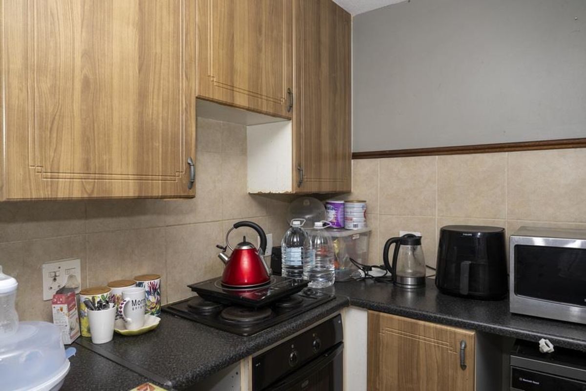 Compact kitchen featuring wood-look cabinetry, dark laminate countertops, and tiled splashbacks, equipped with a built-in oven and hob.