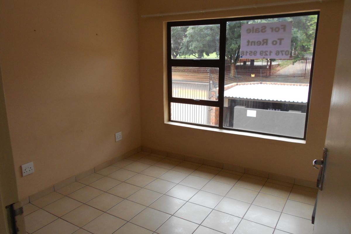 A vacant bedroom featuring neutral tiled flooring, large window with security bars, and standard electrical outlets.