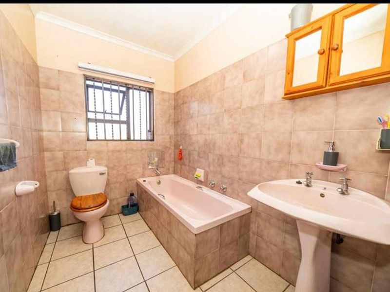 A functional bathroom featuring a pedestal basin, built-in bathtub, and toilet, finished with neutral wall and floor tiling.