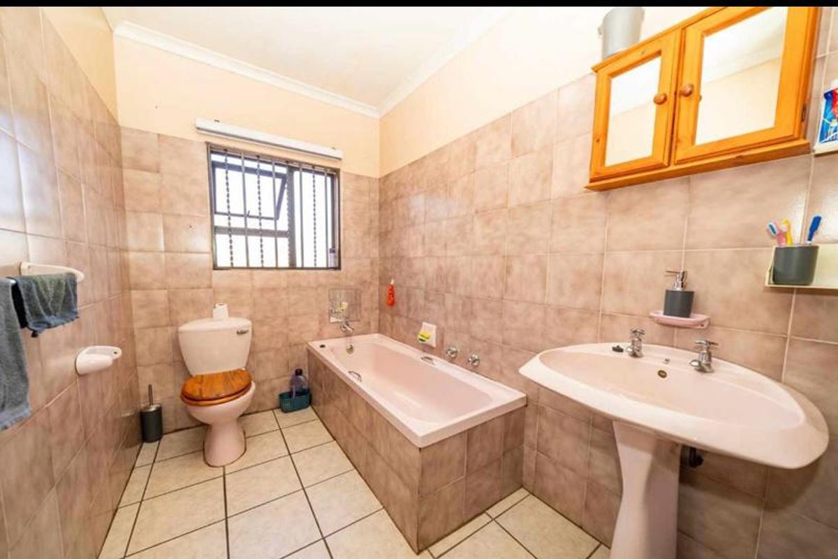 A functional bathroom featuring a pedestal basin, built-in bathtub, and toilet, finished with neutral wall and floor tiling.