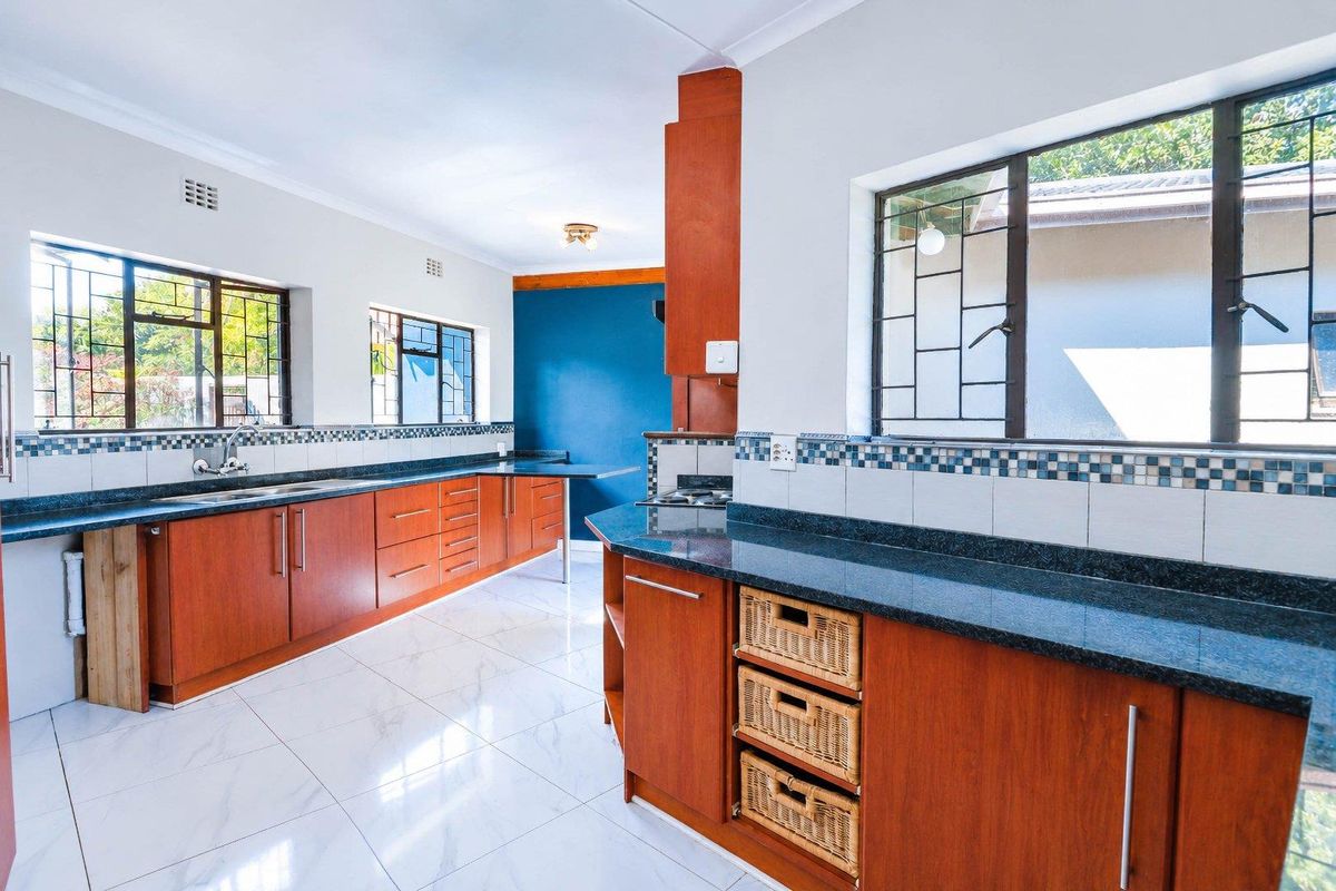 Spacious kitchen featuring wood-finish cabinetry, dark stone countertops, tiled flooring, and large windows with security bars, offering a functional layout.